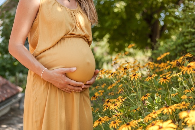 midsection-pregnant-woman-holding-stomach-while-standing-outdoors